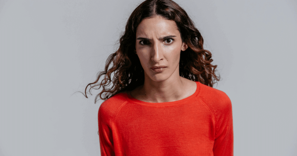 Woman with furrowed brow, depicting subconscious anxiety, stress, and emotional expression. Red sweater, curly hair.